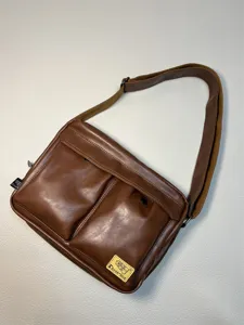Brown PU leather messenger bag detail, showing front dual pockets and branded label design.