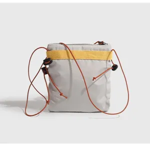 Dettaglio della leggera borsa a tracolla grigia con cinturino giallo e cordoncini regolabili.