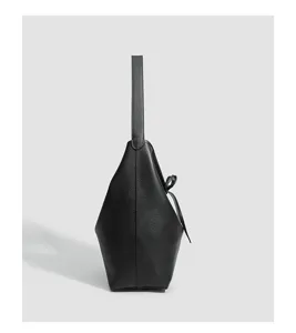 Detalle de perfil lateral en cuero negro del bolso cubo minimalista para estilo diario.