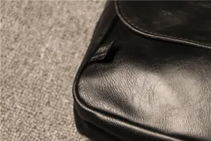 Detailed view of black leather men shoulder bag side tag craftsmanship texture display.