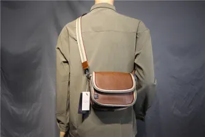 Detail view of the brown messenger bag with striped canvas strap and flap design worn on back.