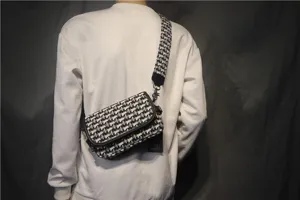Vue détaillée d'un sac bandoulière en toile noire et blanche porté avec une large sangle.