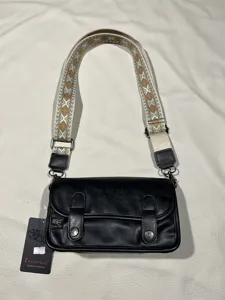 Close-up detail of the retro black crossbody bag showing ethnic woven strap and logo.