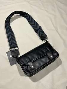 Close-up detail of a retro black messenger bag featuring wide patterned strap and metal buckles.