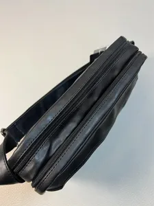 Close-up detail of black men's multi-zipper messenger bag, showing zipper and PU leather.