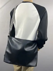Back detail view of black leather messenger bag with patterned wide strap worn by model.