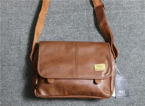 Close-up of brown PU leather messenger bag detail, showing texture, flap and strap hardware.