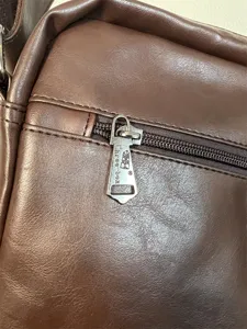 Close-up detail of the brown leather messenger bag zipper and metal pull, stylish daily wear.