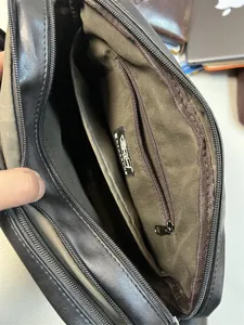 Men's black leather messenger bag interior detail shot showing multiple zipper compartments.