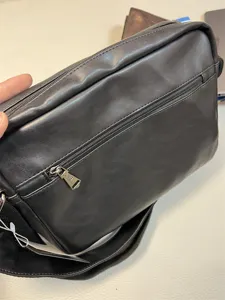Black leather crossbody shoulder bag, detailed view of the front zipper pocket hardware.