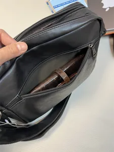 Detail shot of black leather messenger bag with front zipper pocket and metal hardware.