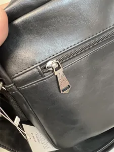Detailed view of black messenger bag zipper and brand tag, durable PU leather material.