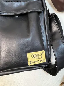 Close-up detail of black leather messenger bag featuring front flap pocket and sturdy strap.