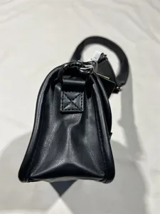 Detail view of black leather crossbody bag side gusset, fine stitching and metal hardware.