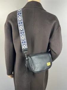 Black leather crescent crossbody bag with stylish wide patterned shoulder strap for daily use.