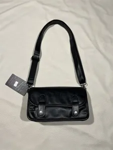 Black leather crossbody bag detail showing adjustable strap, metal snap buttons, and brand logo.