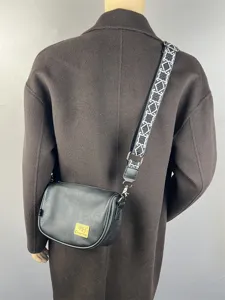 Detail view of black crossbody bag with wide geometric pattern strap and front logo patch.