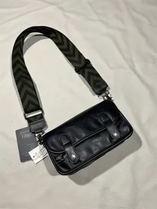Detailed view of black leather messenger bag with adjustable green chevron shoulder strap.