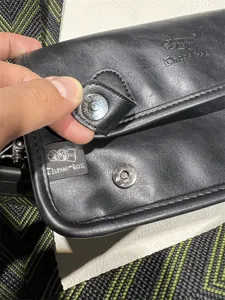 Close-up of black leather messenger bag with magnetic snap and Three-box logo detail.