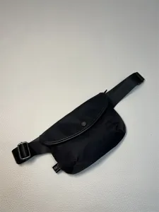 Detailed view of black nylon crossbody bag, adjustable strap, metal buckle and flap design.