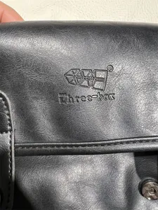 Detail shot showing the embossed Three-box brand logo and premium faux leather texture.