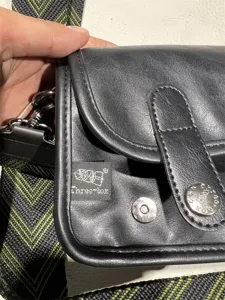 Black vintage crossbody bag detail shot, showing textured strap and metal snap closure.