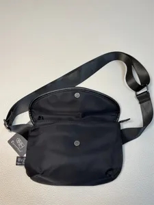 Close-up detail of black nylon crossbody bag with adjustable wide strap and metal snap closure.