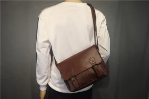 Detail view of the vintage brown leather messenger bag with double buckles worn crossbody.