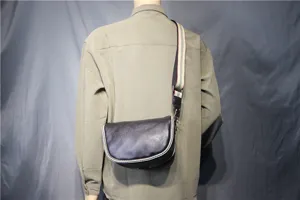 Detailed view of the black leather saddle bag worn across the body, featuring striped strap.