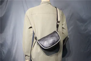 Detail view of the black leather cross-body saddle bag worn, showing its shape and striped strap.