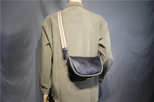 Detailed view of the men's leather saddle bag worn across the body with a striped strap.