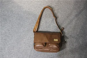 Close-up detail of the brown leather messenger bag featuring front pockets and adjustable strap.