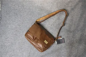 Brown leather messenger bag detail showing flap pocket, adjustable strap and metal logo.