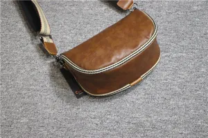 Detailed close-up view of a brown vintage saddle bag featuring striped webbing trim and wide strap.