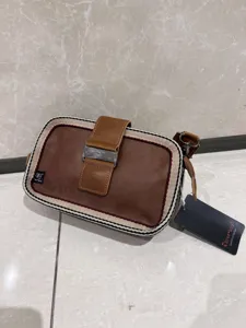 Retro striped canvas and brown leather crossbody bag detail view with metal buckle closure.