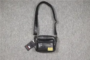 Vue détaillée du sac bandoulière en cuir noir avec poches zippées et sangle réglable.