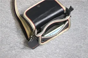 Black cross-body bag with striped canvas straps and multi-compartment interior storage design.