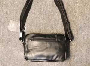 Close-up detail of the black leather cross-body bag zipper pocket and brand hangtag.