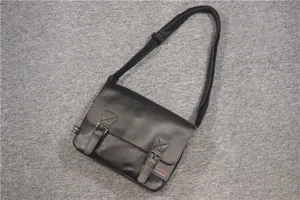 Close-up detail shot of the black leather messenger bag featuring durable metal buckles and strap.
