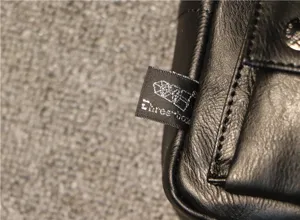 Close-up view of the black leather bag showcasing the brand tag, detailed stitching, and snap.