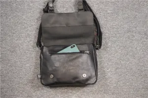 Detail view of black faux leather messenger bag, showing zipper pocket, flap and metal hardware.