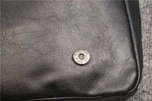 Close-up detail of black leather messenger bag featuring metallic magnetic snap button.