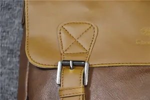 Close-up detail of vintage leather messenger bag strap, metal buckle and stitching.