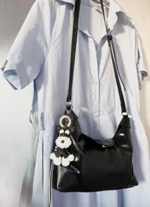 Detailed shot of black shiny shoulder baguette bag with cute dog keychain, daily commuter style.