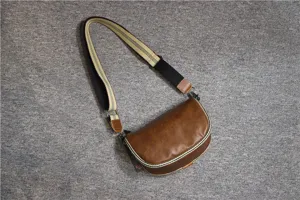 Details of brown leather retro saddle bag with wide strap, textured surface and stitching.