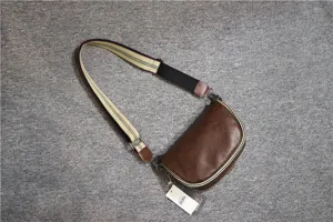 Brown leather saddle bag detail showing striped canvas strap and fine hardware design.