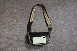 Detail view of a minimalist black leather saddle bag with wide striped canvas strap for men.