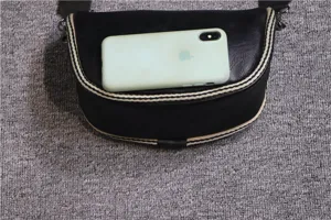 Black leather saddle bag with striped trim, shown with phone for size reference detail.
