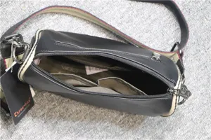 Detail view of black cylindrical crossbody bag with open zipper, inner compartments and strap.