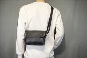 Detail view of a black flap messenger bag worn on back, showing compact urban style.